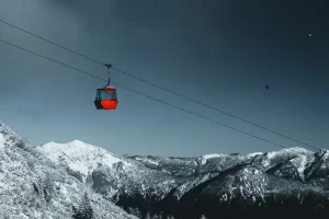 Red cable car in Austria ascending a steep mountain with hot air balloons in the back