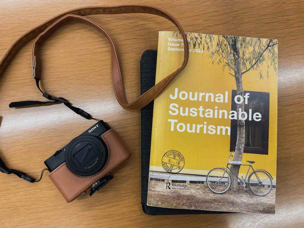 Camera and books on a table with the title 'Journal of Sustainable Tourism'