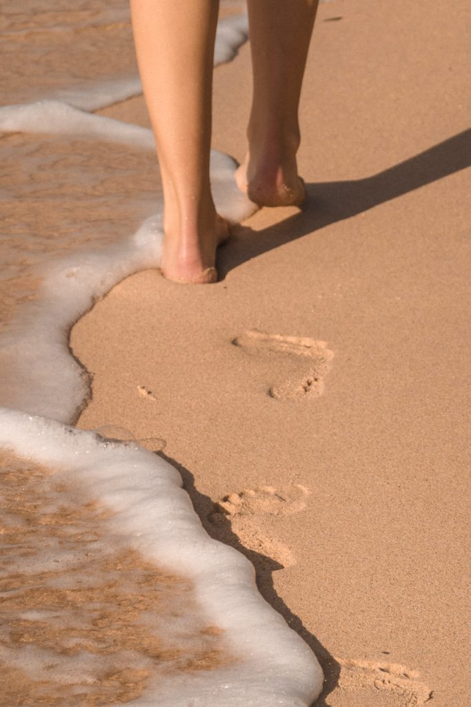 Footprints in the sand from a woman walking away with waves rolling in