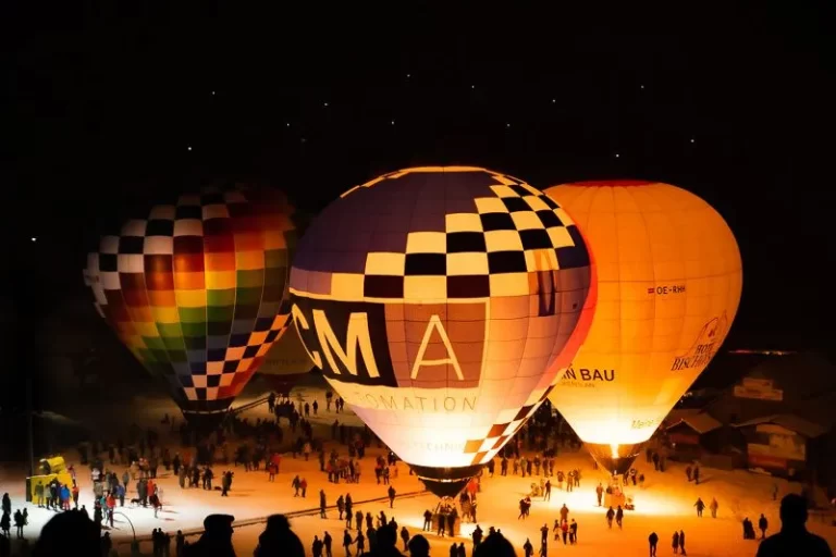 Three hot air balloons lit up at night while tethered to the ground