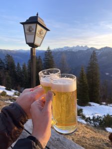 Two hands holding beers together on a mountain top in winter