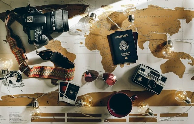 Assortment of travel items including a camera, passport, compass, photos, and a notebook laid out of a brown and white map