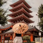 Girl standing with a paper umbrella in front of a temple in Japan